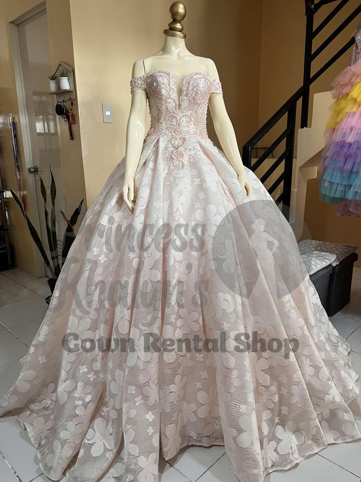 Blush pink off-shoulder ball gown with heart-shaped bodice, intricate lace embroidery, and large floral patterns on the skirt