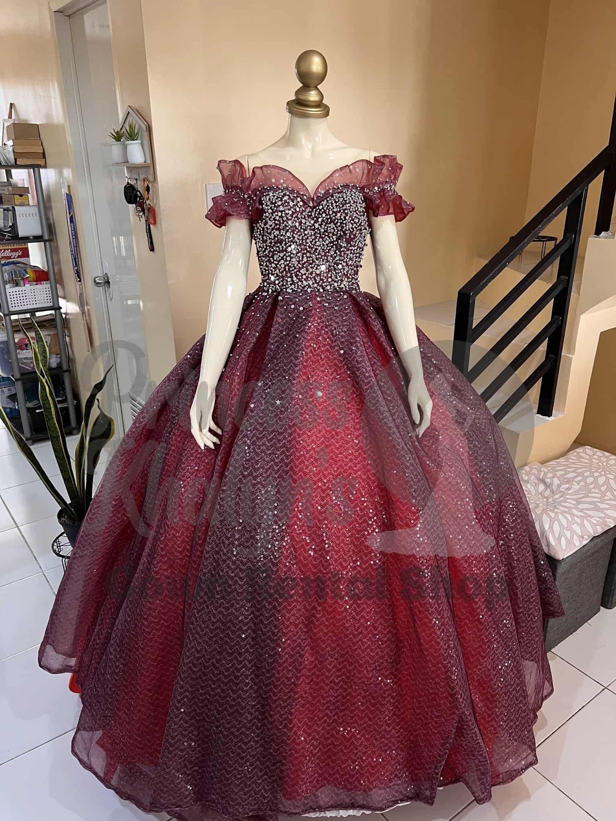 Burgundy ball gown with ruffled off-shoulder sleeves, sequin-embellished bodice, and glittering layered skirt