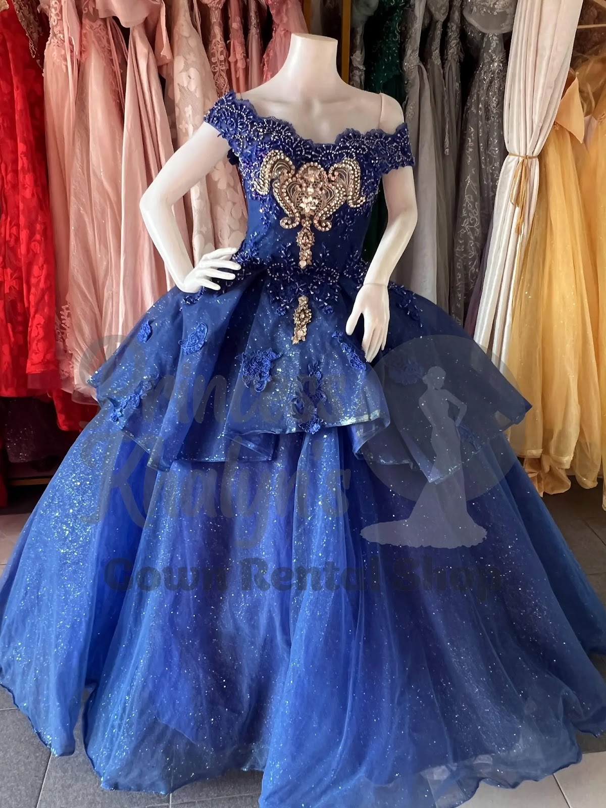 Deep blue off-shoulder ball gown with ornate gold beadwork, floral appliqué, and glittery layered skirt