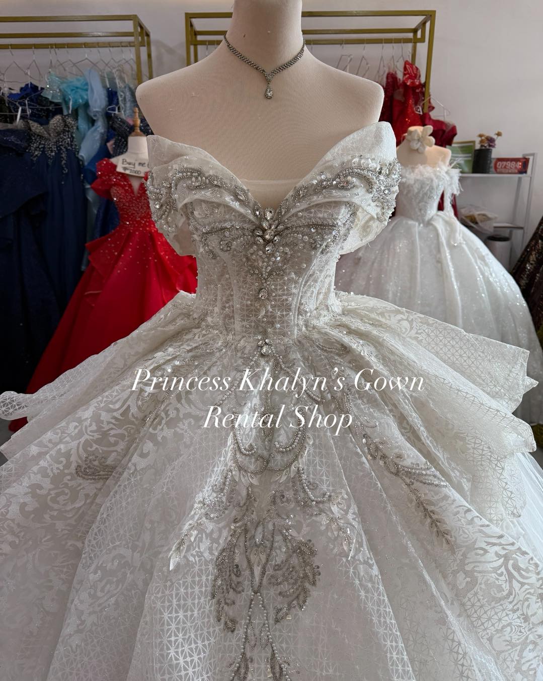A stunning white off-shoulder ball gown featuring intricate silver beadwork and embroidery on the bodice, with a voluminous patterned tulle skirt. The gown exudes elegance and sophistication, perfect for formal occasions.