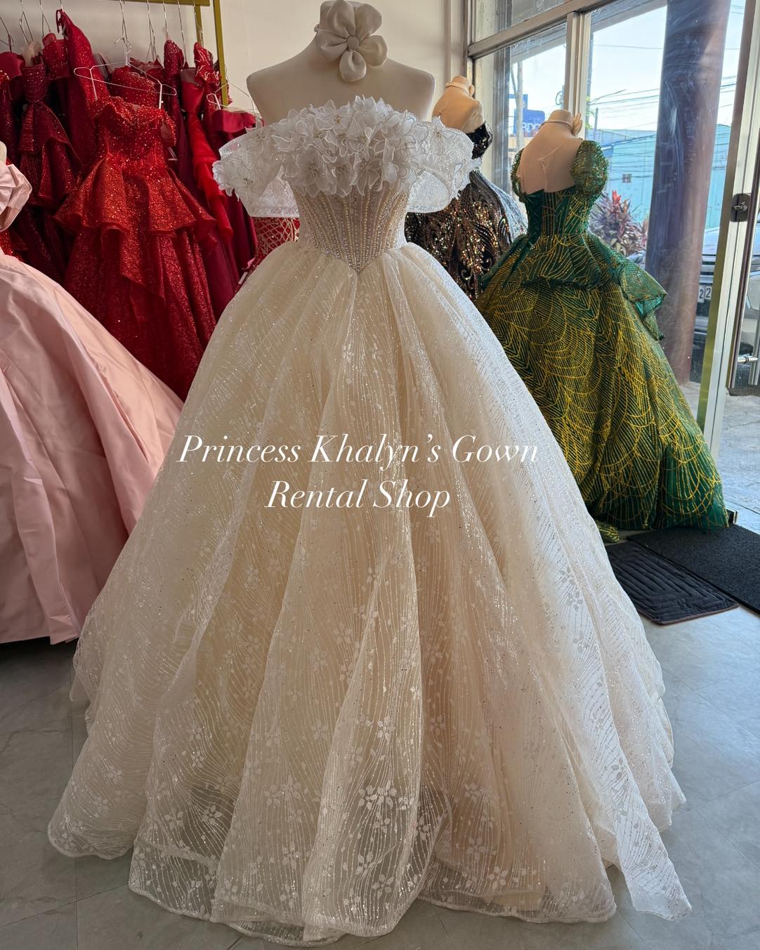 Ivory off-shoulder ball gown with intricate floral appliqué on the bodice, a voluminous shimmering skirt, and delicate ruffle detailing.