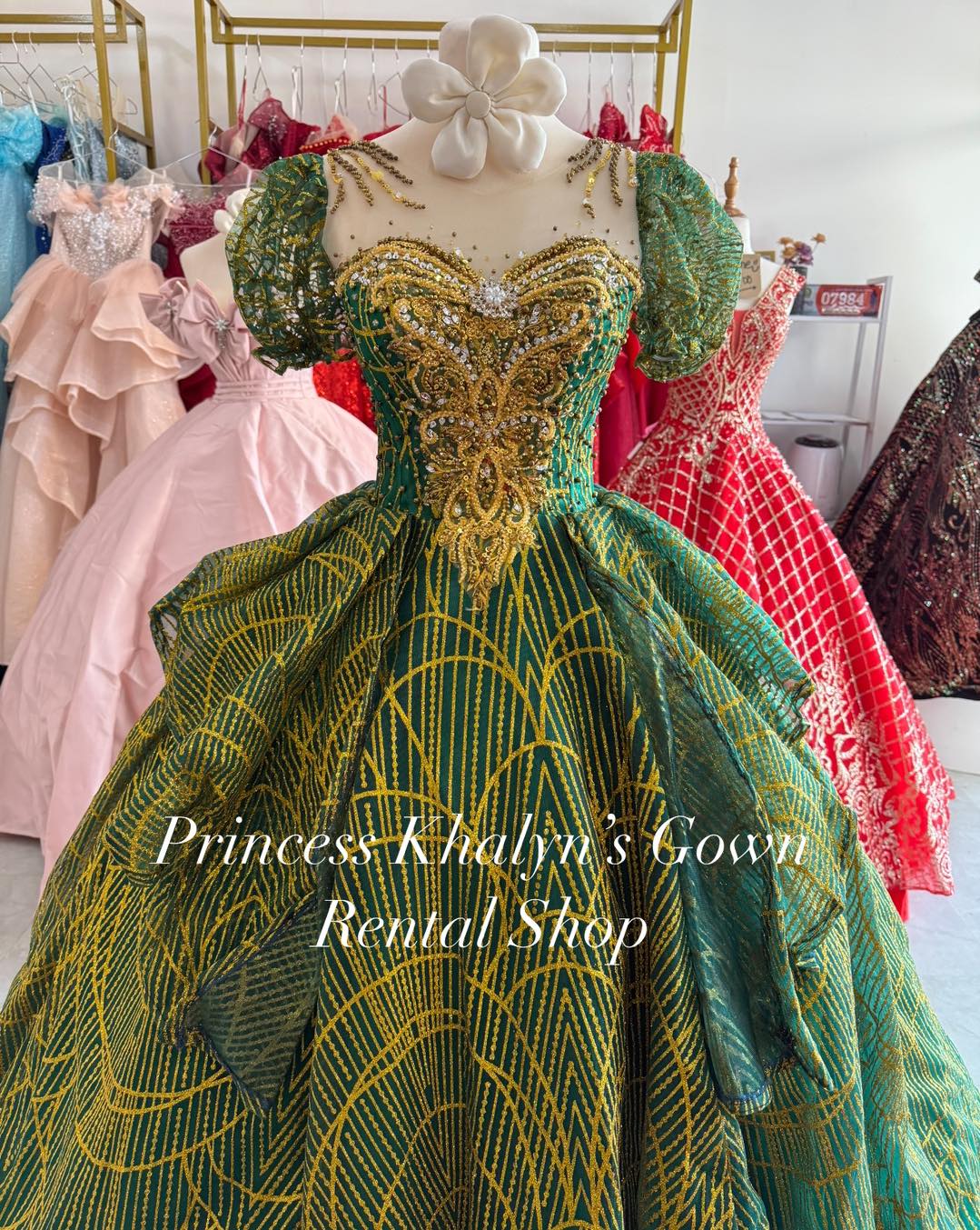 An elegant green ball gown with puffed sleeves and intricate gold embroidery on the bodice. The gown features a full skirt with a geometric pattern and shimmering beadwork, creating a luxurious and regal appearance.