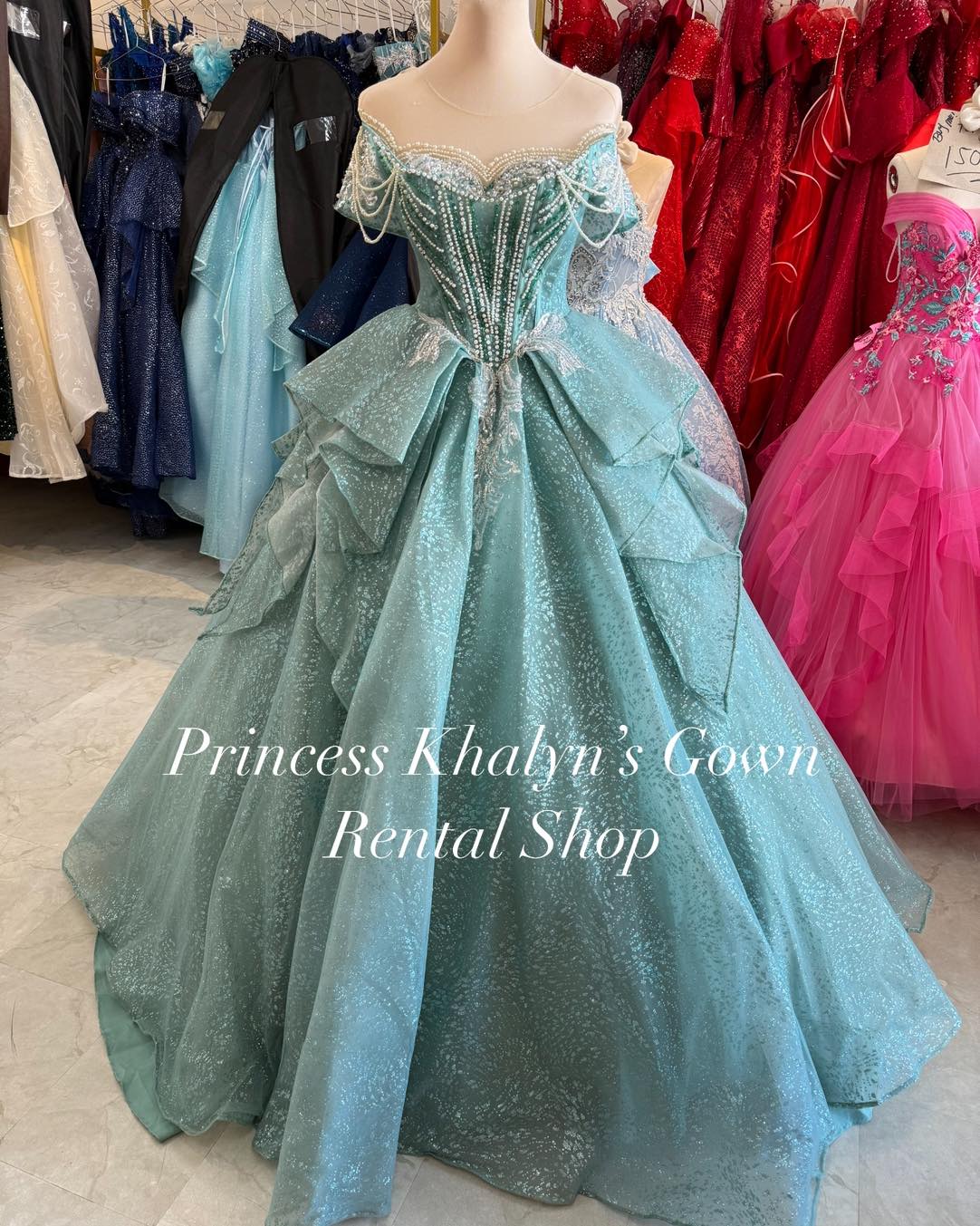 A stunning aqua green off-shoulder ball gown with intricate pearl and lace detailing on the bodice, featuring cascading layers and a shimmering textured skirt.