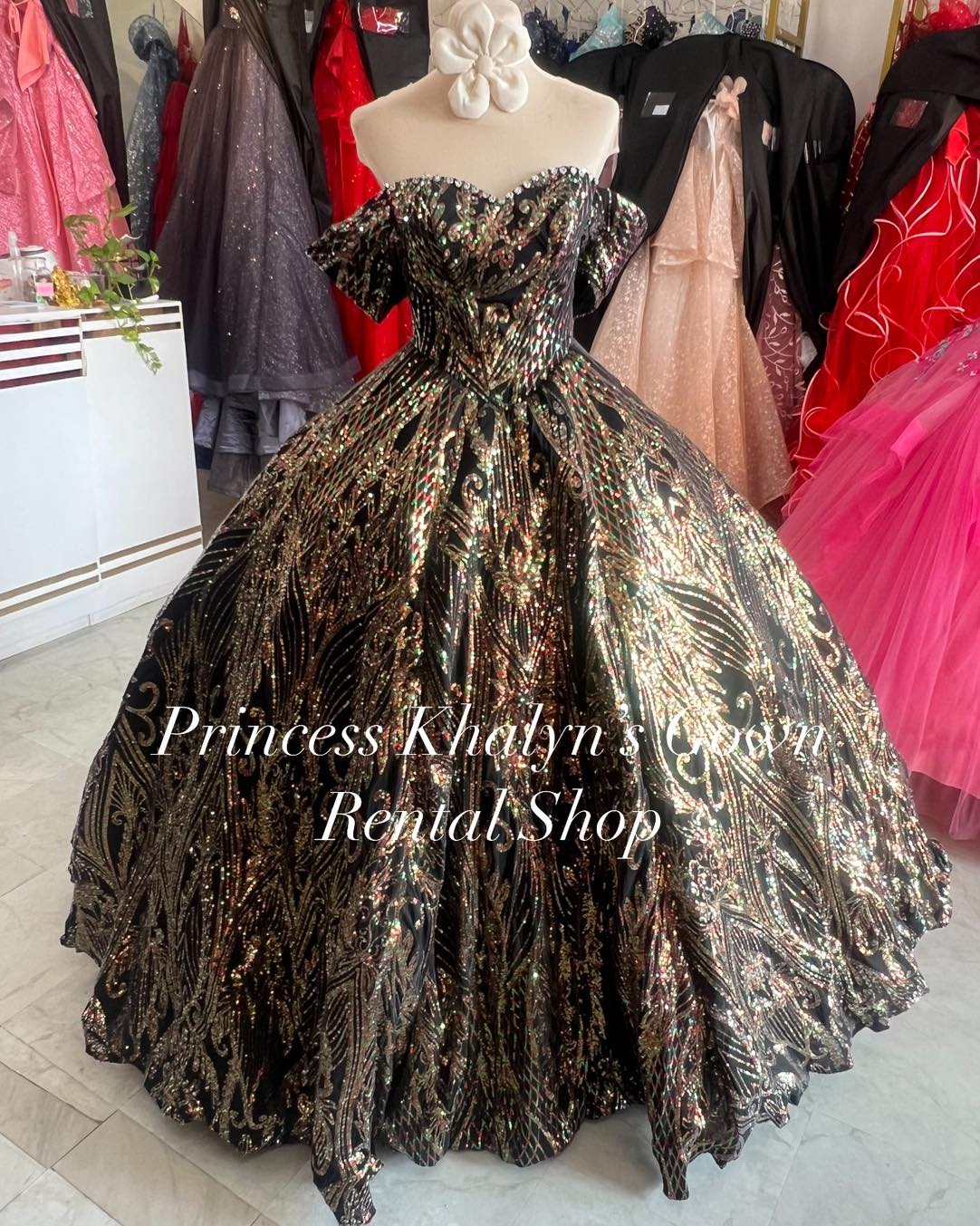 A luxurious black off-shoulder ball gown with intricate gold and silver sequin embroidery creating a dazzling pattern. The gown features a fitted bodice and voluminous skirt, perfect for making a grand entrance at any formal event.