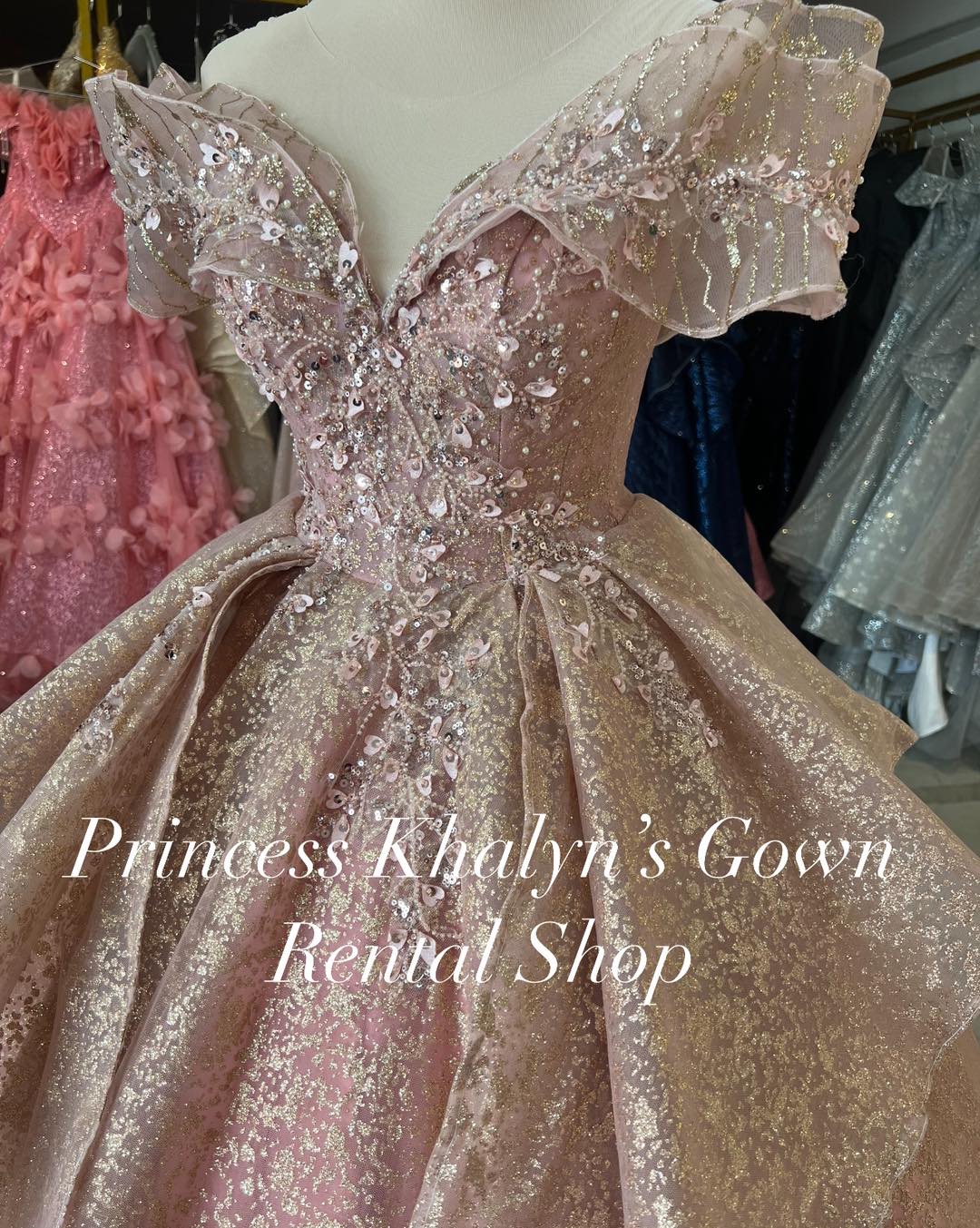 A stunning pink ball gown with off-shoulder design, featuring intricate floral appliqué and shimmering sequins. The gown has a voluminous skirt with a glittery finish, creating an elegant and enchanting appearance.