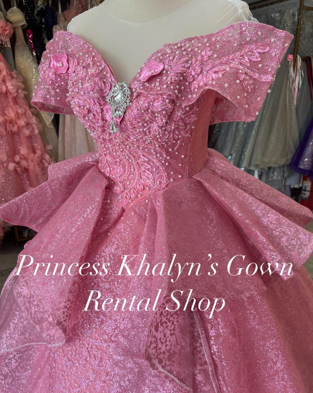 A pink off-shoulder gown with intricate beadwork and floral appliqué on the bodice, featuring a voluminous shimmering skirt and delicate ruffle detailing.