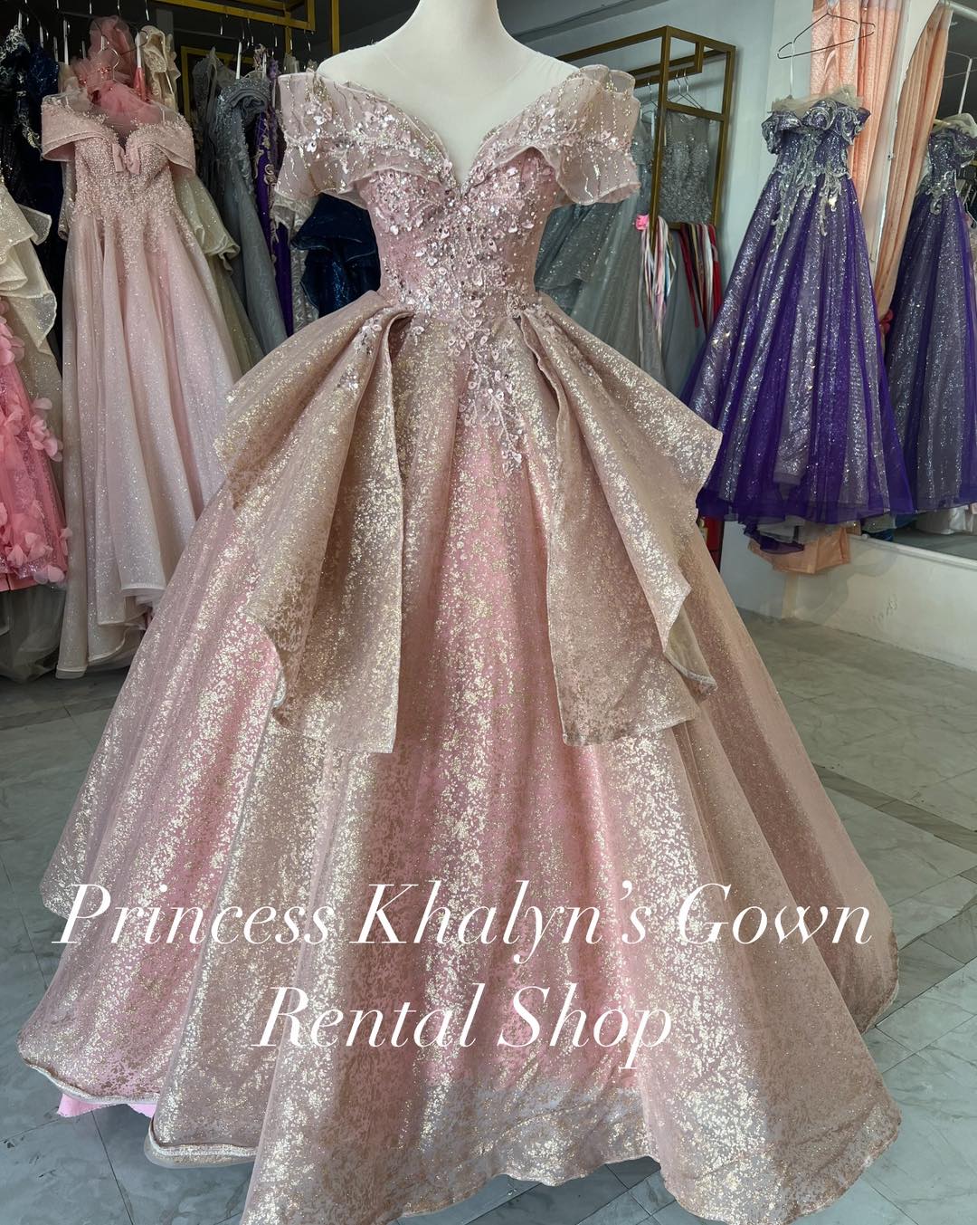 A shimmering pink off-shoulder ball gown with intricate sequin embellishments and a voluminous skirt. The gown features delicate ruffled sleeves and a fitted bodice adorned with sparkling details, creating an elegant and glamorous appearance.
