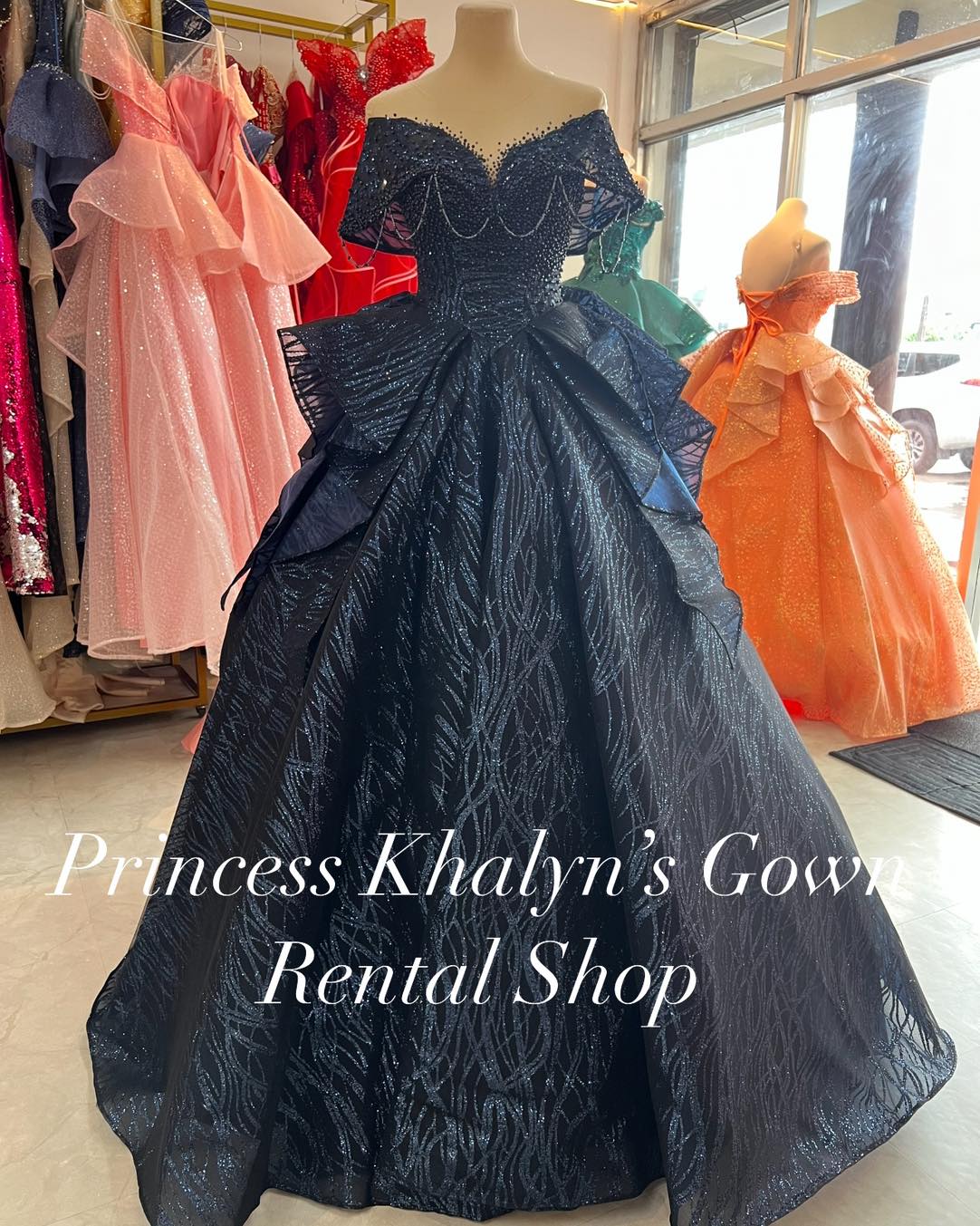 A black off-shoulder ball gown with intricate beadwork on the bodice and a voluminous textured skirt. The gown features elegant draping and a shimmering pattern, perfect for formal occasions.