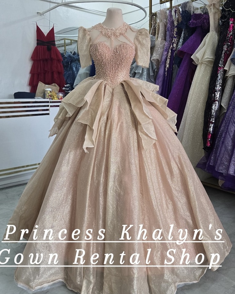 A luxurious champagne-colored ball gown with a shimmering bodice adorned with intricate beadwork. The gown features puffed sleeves, a high neckline with delicate embellishments, and a voluminous layered skirt with a cascading ruffle design, creating an elegant and regal appearance.