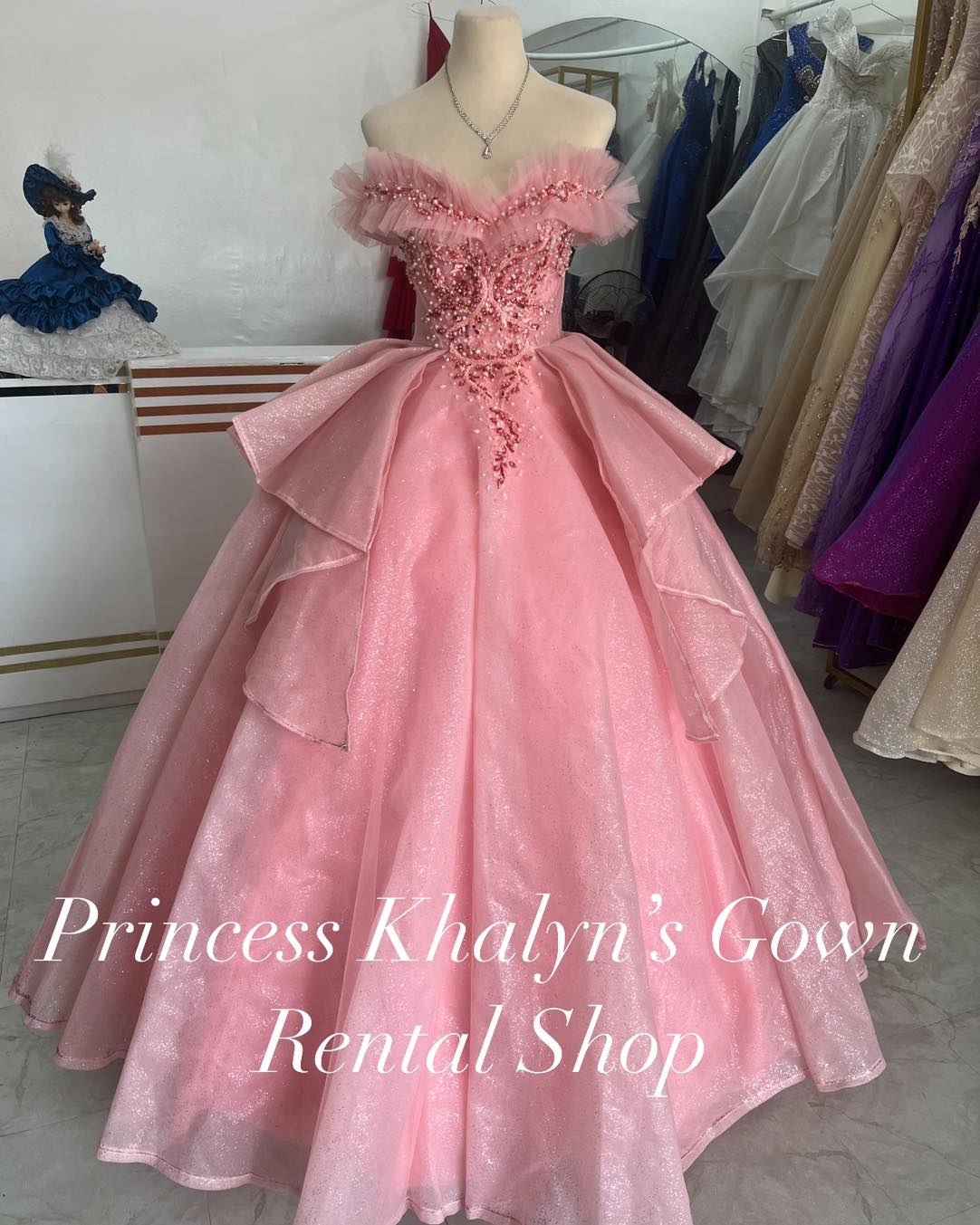 A stunning pink off-shoulder ball gown with a shimmering bodice adorned with intricate beadwork and ruffled tulle detailing. The gown features a voluminous layered skirt with a sparkling finish, creating an elegant and enchanting look.