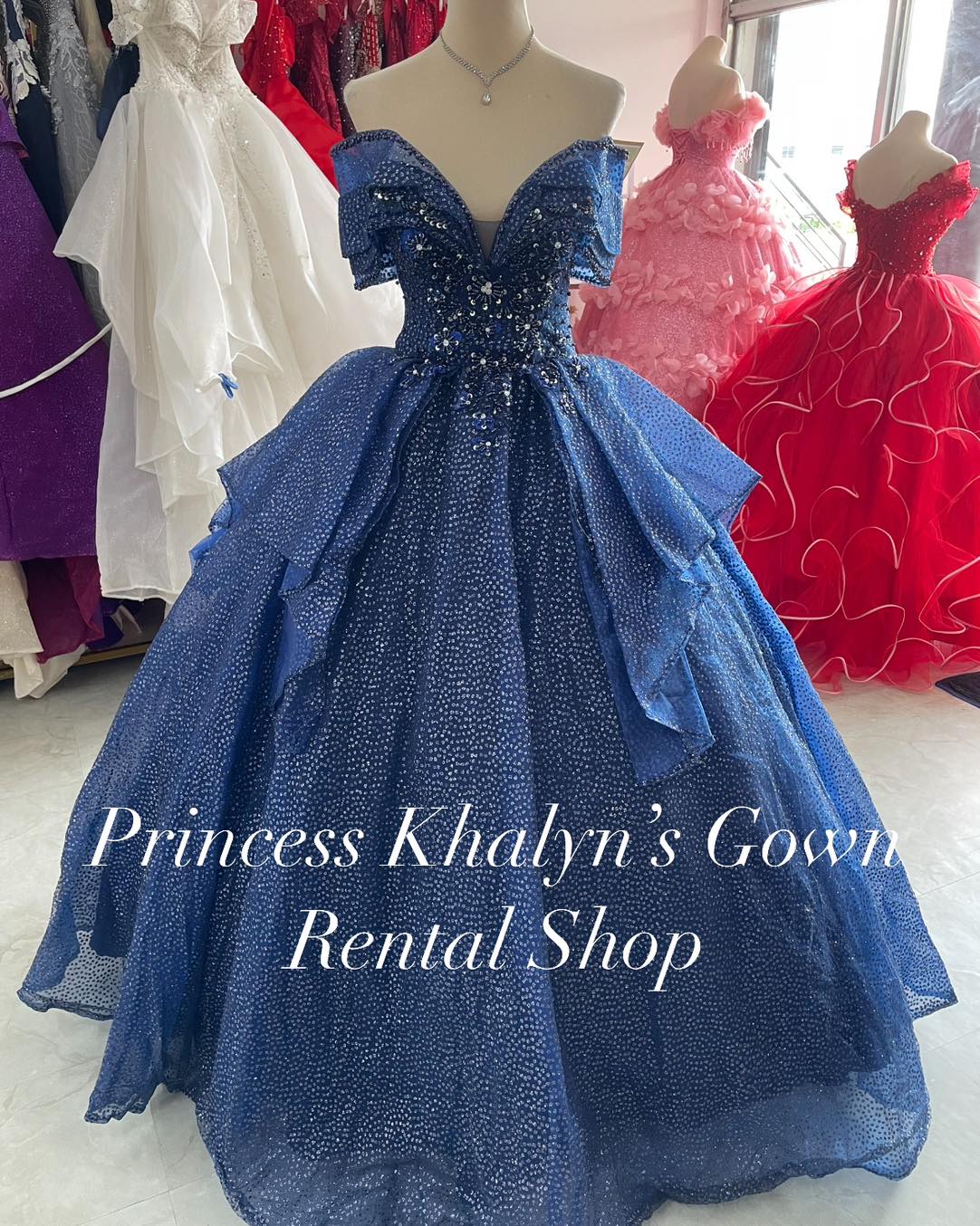 A dazzling blue off-shoulder ball gown with intricate beadwork on the bodice and a voluminous tulle skirt. The gown features a shimmering dotted pattern throughout, creating a sparkling effect.