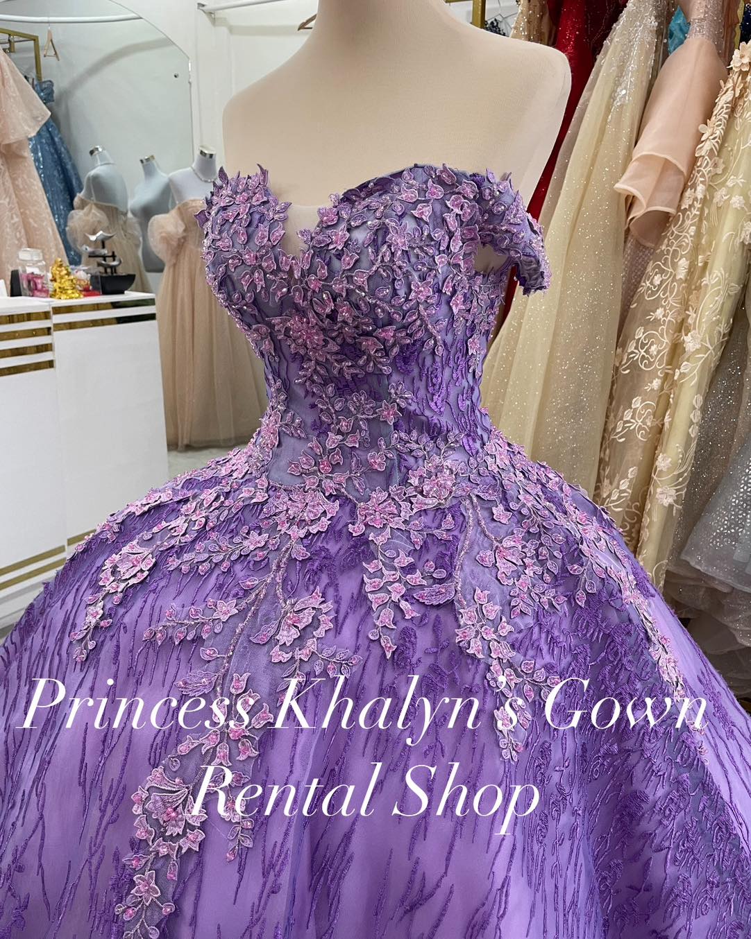 A stunning purple off-shoulder ball gown adorned with intricate pink floral appliqué and a voluminous skirt, perfect for elegant events.