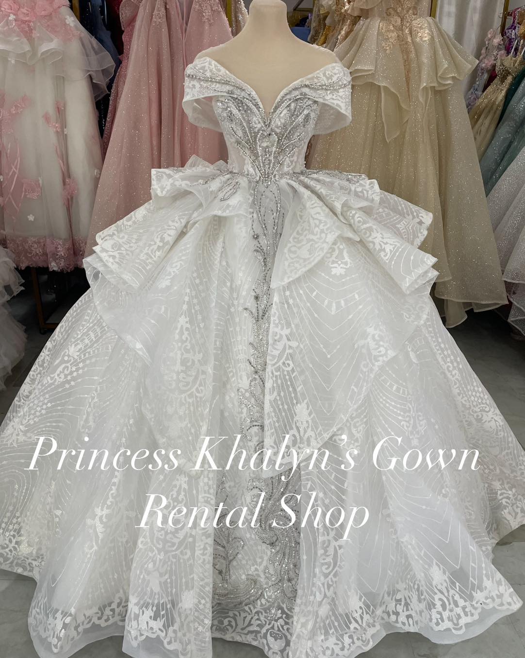 A luxurious white off-shoulder ball gown with intricate silver embroidery and a voluminous layered skirt. The bodice features elaborate beadwork, creating a sophisticated and regal appearance.