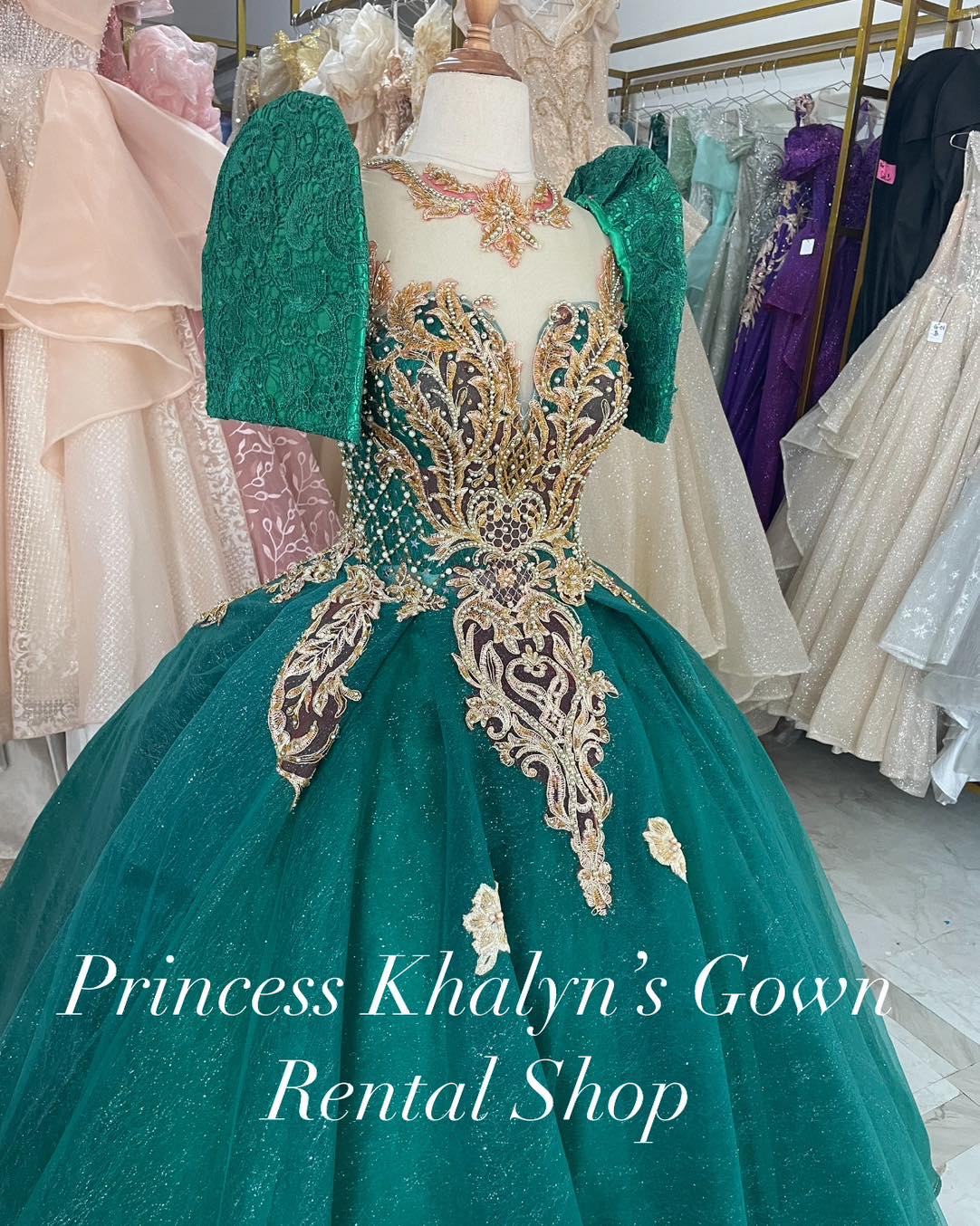 A luxurious emerald green ball gown with puffed lace sleeves and intricate gold embroidery on the bodice. The gown features a voluminous skirt adorned with shimmering details, creating an elegant and regal appearance.
