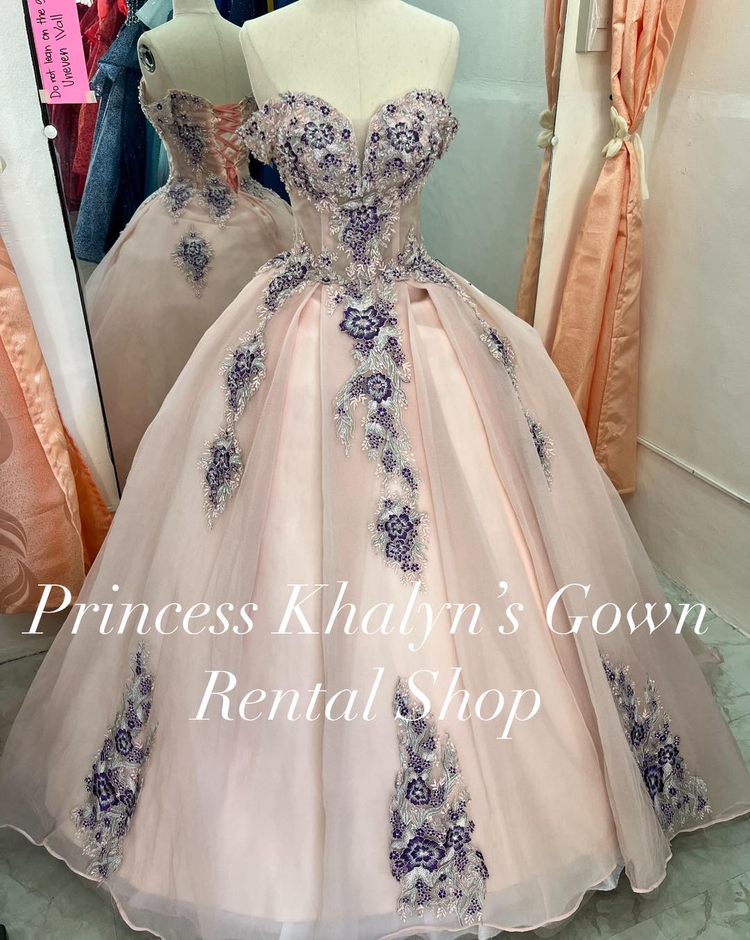 A blush pink ball gown with a sweetheart neckline, adorned with intricate lavender floral embroidery and beadwork. The gown features a fitted bodice and a voluminous skirt, creating an elegant and sophisticated look.