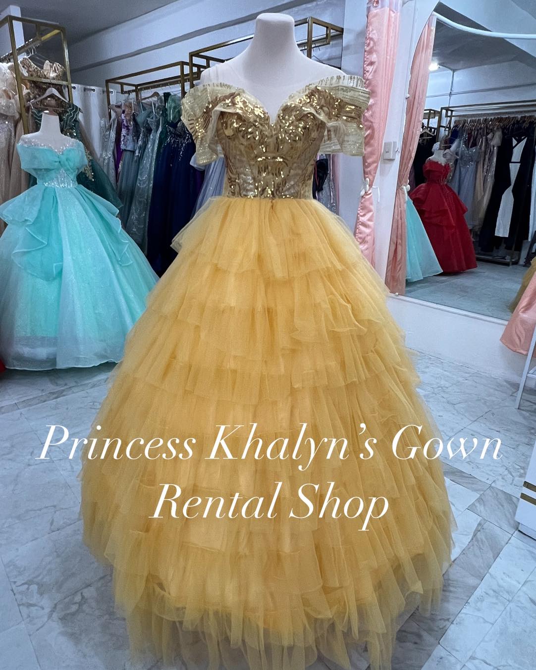 A gold off-shoulder ball gown with a shimmering sequined bodice and layered ruffle tulle skirt, exuding elegance and glamour.