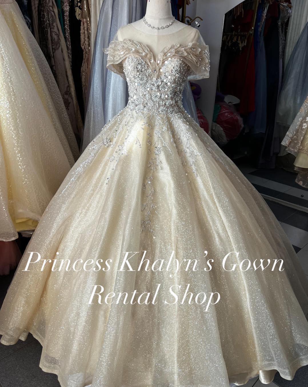 A luxurious gold ball gown with off-shoulder design, intricate floral embroidery, and a shimmering full skirt. The bodice features delicate beadwork and the gown exudes elegance, suitable for formal occasions.