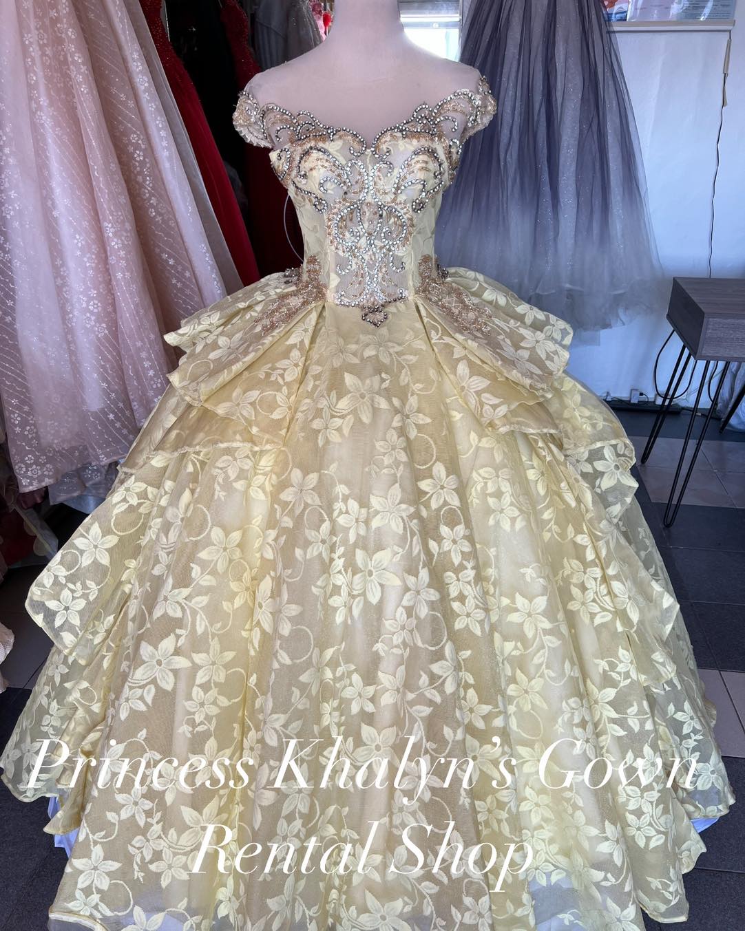 A gold off-shoulder ball gown with intricate beadwork and floral embroidery on the bodice, featuring a layered skirt with floral patterns, creating an elegant and sophisticated look.