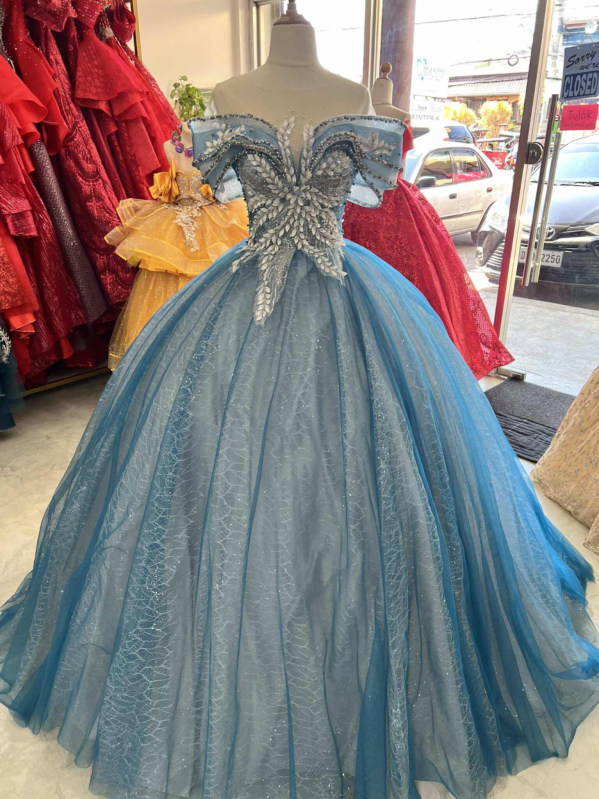 This stunning blue gown features an off-shoulder design with intricate embellishments and a voluminous skirt, perfect for making a grand entrance at any formal occasion.