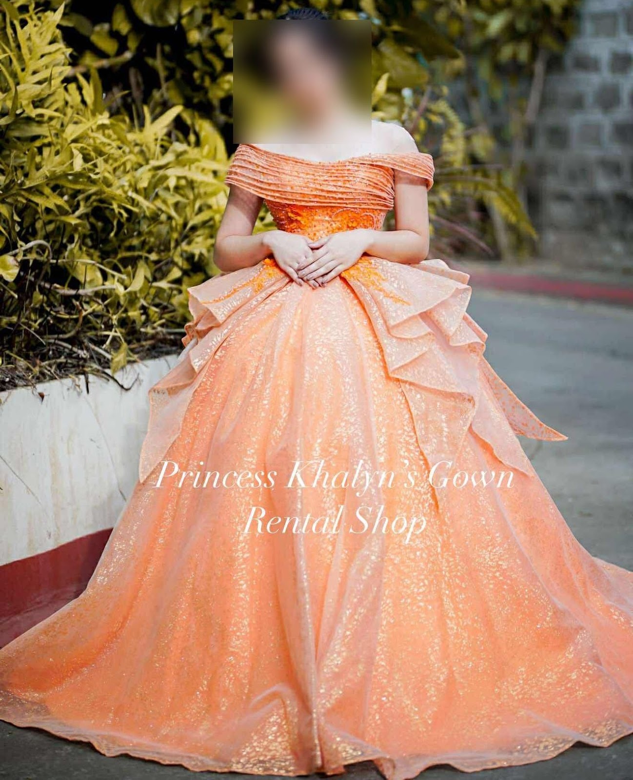 An elegant peach gown featuring a structured off-shoulder neckline and a voluminous layered skirt, adorned with shimmering accents for a captivating look.